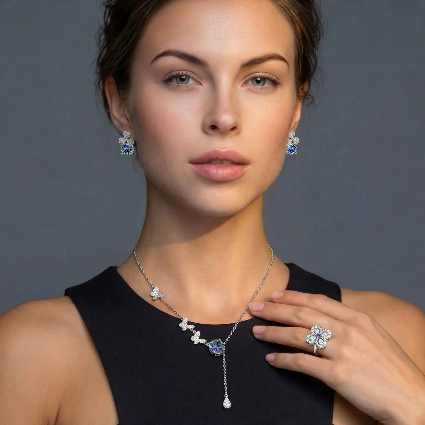 Woman wearing butterfly-themed jewelry including necklace, earrings, and ring on a gray background