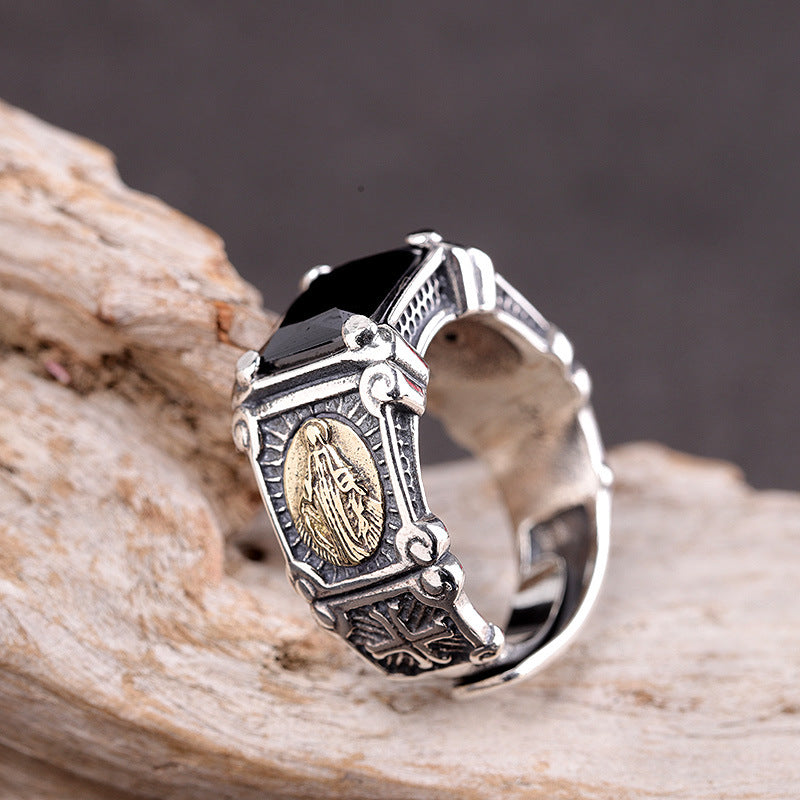 Silver ring with black gemstone and religious emblem on a wooden surface