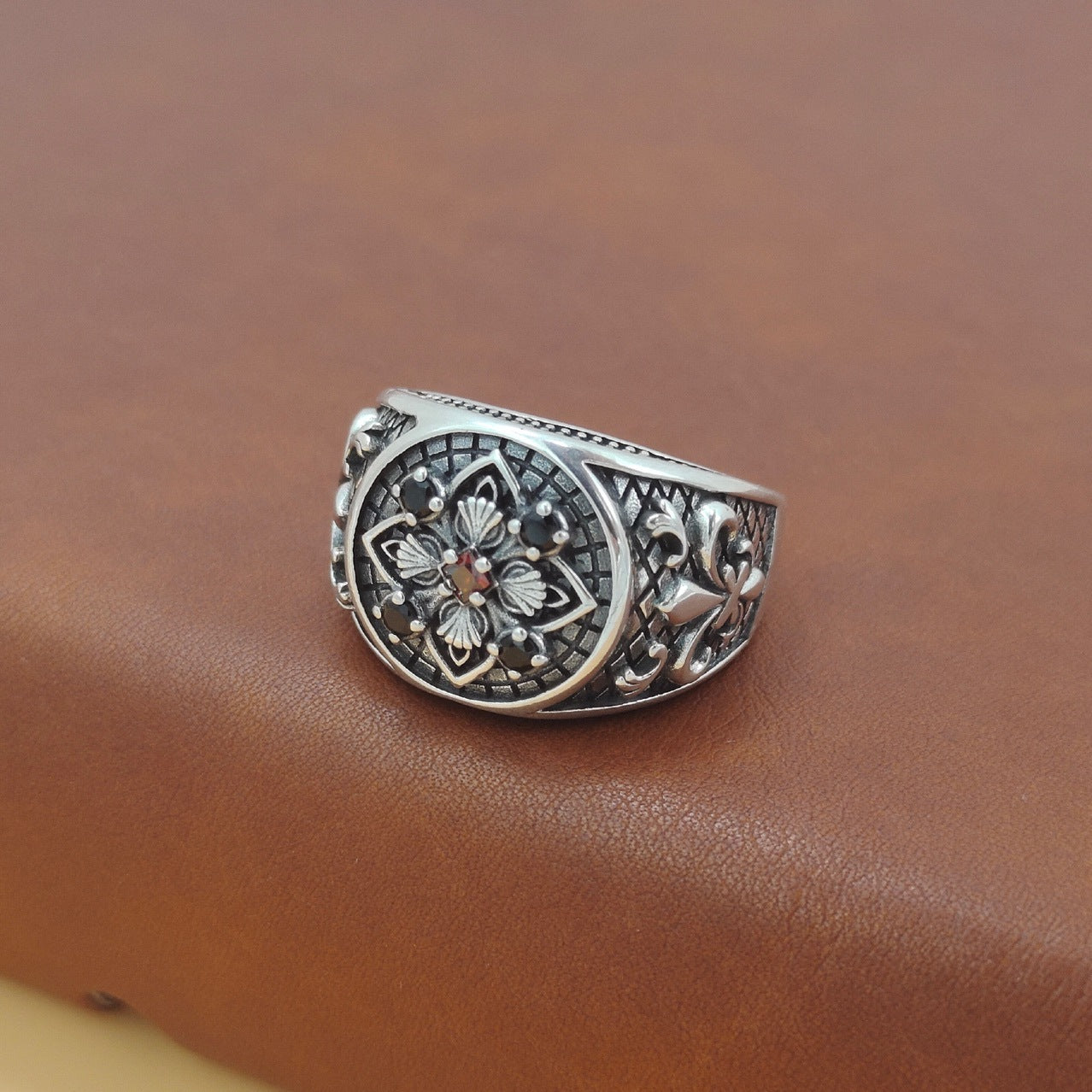 Silver ring with intricate design on a brown leather surface